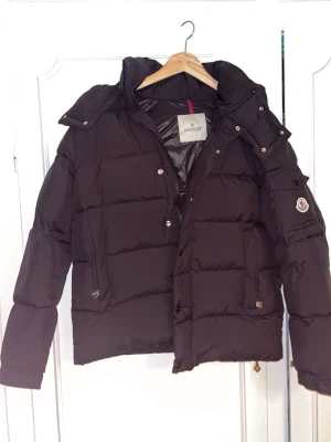 Moncler Vezere pufferjacka - Säljer en svart pufferjacka från Moncler med klassisk logga på ärmen och dragkedja framtill. Jackan har hög krage, avtagbar huva och flera fickor med både dragkedja och knappar. Storlek 2, passar M. 