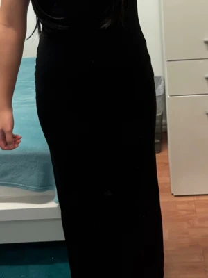 Svart långklänning i stretchigt tyg - Säljer en svart långklänning med figurnära passform. Klänningen är ärmlös och har en enkel, stilren design utan mönster eller detaljer. Tyget är mjukt och stretchigt vilket gör den bekväm att bära. Perfekt för dig som gillar minimalistisk stil.