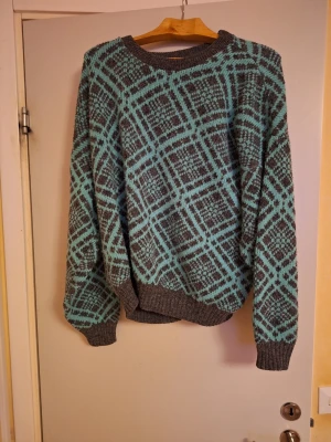 Gråblå stickad tröja med rutmönster - Säljer en stickad tröja i grått och ljusgrön med rutigt mönster. Tröjan har rund halsringning, ribbade muddar och lång ärm. Perfekt för dig som gillar retrovibbar och vill ha något unikt i garderoben.