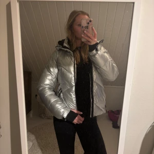 Silvrig dun skidjacka - En silvrig dun skidjacka från McKinley storlek 38. Finns snölås, ficka för liftkort på armen och innerfickor alltså perfekt för skidåkning! Använd fåtal gånger så i väldigt fint skick.