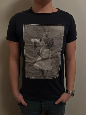  Limitato T-shirt - Svart t-shirt från Limitato med ett stort svartvitt fotoprint på bröstet som föreställer ett barn som dricker ur en burk. T-shirten har rund halsringning och korta ärmar. Skön och stilren modell som sticker ut med sitt unika tryck. Ny pris 1500 kronor ungefär boxen med följer ej tyvärr. Kom privat för pris om priset är för högt. 