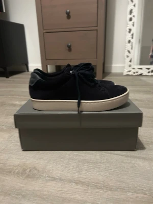 Mörkblå sneakers från Vagabond, strl 37 - Snygga mörkblå sneakers från Vagabond i mocka med vita, platta sulor och klassisk snörning. Skorna har rund tå och diskret Vagabond-logga bak på hälen. Perfekta till jeans eller kjol för en clean och stilren look.