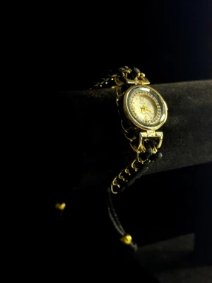 Obsidian Timepiece – Chain Edition - Obsidian Timepiece – Chain Edition är en elegant och unik armbandsklocka som kombinerar klassisk guldfinish med ett dekorativt kedjeinspirerat armband i svart och guld. Den runda urtavlan med gnistrande detaljer ger ett exklusivt och smyckeslikt uttryck, perfekt för dig som vill bära något utöver det vanliga. Klockan är lätt, bekväm och fungerar lika bra som accessoar till vardags som till fest. Helt ny och redo att användas eller ges bort som present.