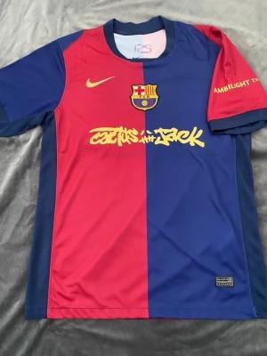 FC Barcelona Nike matchtröja Lamine Yamal - Säljer en officiell FC Barcelona matchtröja från Nike med Lamine Yamal och nummer 19 på ryggen. Tröjan är röd och blå med gul Nike-logga, klubbmärke och tryck. Tillverkad i lätt polyester, perfekt för fotboll eller samling. Snygg detalj med Cactus Jack-logga på bröstet.