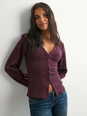 Waist focus cardigan från Nelly - Säljer en vinröd blus med v-ringning och långa ärmar. Blusen har en figurnära passform och knäppning framtill. Perfekt att styla med jeans för en snygg look. Materialet känns mjukt och följsamt. Är bara använd någon gång och är i nyskick. Storlek Xxs