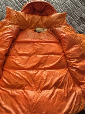 Nunatak pufferjacka från Axel Arigato i färgen orange  - Säljer en riktigt fet orange pufferjacka från Axel Arigato. Jackan har en glansig finish, stor huva och dragkedja framtill. Två fickor med dragkedja på sidorna och tydlig logga på bröstet. Perfekt för kalla dagar när du vill sticka ut pufferjackan kostar  runt 9500kr ny modellen är S men passar som en M