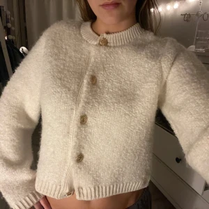 Vit kofta med guldknappar - Säljer en superfin vit kofta med guldknappar. Den har en mysig, fluffig textur. Perfekt för höst och vinter, och den är i mycket bra skick. Passar perfekt till både vardag och festliga tillfällen!