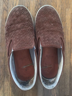 Vin röda mocka slip-on från Bottega Veneta - Säljer ett par vin röda slip ons från bottega veneta i storlek 42, skorna är väldigt fina, skorna är rätt använda har haft de under två somrar, därför säljs skorna för så lite skorna är i ett väldigt fint mocka tyg, skorna kräver lite vård, skorna har några få defekter några sömmar har gått sönder som finns på nån bild. sulorna är också använda därför rekommenderars det att byta sula då orginal sulan är rätt använd, gårattfixa, skorna är köpta för 3700 kr det kommer med en dust bag till skorna😀