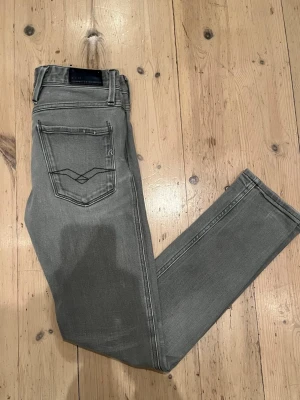 Grå replay anbass jeans - Snygga grå jeans från Replay med slim fit passform och klassisk femficksdesign. De är storlek 30W 34L men jag skulle säga att de sitter mer som 29W 32L. Byxorna har svarta detaljer, diskret Replay-logga och raka ben. Jeansen är i otroligt bra skick utan några hål eller defekter. Materialet är mjukt jeans med stretch för extra komfort. Perfekt för dig som gillar stilrena och moderna jeans. Vid frågor eller funderingar hjälper jag gärna till 