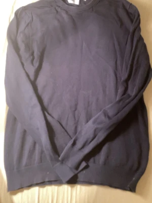 Mörkblå stickad tröja från Bläck - En enkel och stilren mörkblå stickad tröja från Bläck. Tröjan har rund halsringning och ribbade muddar vid halsen. Perfekt till lager på lager under höst och vinter. Passar dig som gillar klassisk och clean stil.