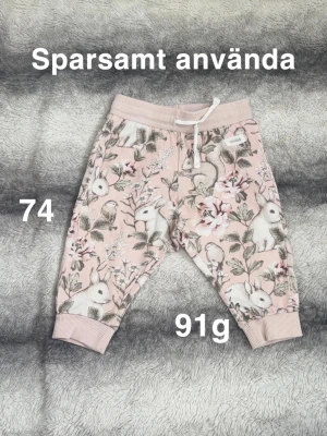 Rosa mjukisbyxor med kaninmönster - Supersöta rosa mjukisbyxor från Newbie med gulligt kanin- och blommönster. Byxorna har ribbade muddar, snörning i midjan. Perfekta för lek och mysiga dagar hemma.🌸 Sparsamt använd. Storlek 74
