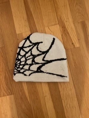 Mössa med spindelnätsmönster - Vit mössa med ett fint spindelnätsmönster runt hela. Mössan är stickad. Perfekt för vintern och passar många olika stilar. Även tjejer och killar har mössan i stil 