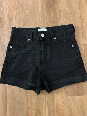 Svarta high waist jeansshorts - Säljer ett par svarta högmidjade jeansshorts med slitningar både fram och bak. Aldrig använda utan bara testade. Perfekt för sommaren!
