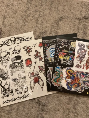  Låtsas tatueringar  - Bilderna visar ark med temporära tatueringar i olika motiv som dödskallar, drakar, örnar och rosor.