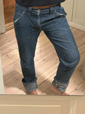J.Lindeberg blå jeans med detaljer - Blå jeans från J.Lindeberg med coola kontrastsömmar och unika fickdetaljer. Klassisk femficksmodell med raka ben och uppvikta benslut. Snygg patch bak och tydliga stickningar ger extra edge. 
