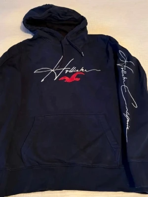 Hollister Hoodie Mörkblå - En vårig och vinterig mörkblå Hollister hoodie med en archive känsla. Bara att skriva om ni har några frågor.