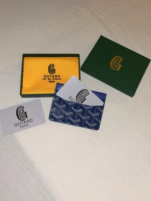 Blå G@yard korthållare i skinn - Säljer en blå korthållare från G@yard med ikoniskt mönster i vitt och brunt. Tillverkad i skinn och har flera fack för kort. Kommer med original grön ask och gul putsduk. Perfekt för dig som vill ha något lyxigt och stilrent i fickan.