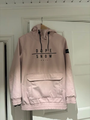 Dope Snow skidjacka - Säljer en ljusrosa skaljacka från Dope Snow med stor magficka, huva med svarta snören och tryck på bröstet. Den är sparsamt använd och i storlek xs. 