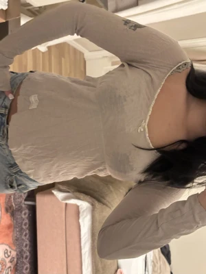 Beige långärmad topp - Supersöt beige långärmad topp från Odd Molly med v-ringning, liten rosett och spetskant vid halsen. Tryck med fågel och logga på ena ärmen. Tunn och mjuk i bomull, perfekt till jeans eller kjol.