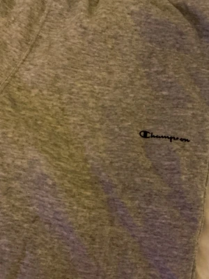 Grå mjukisbyxor från Champion - Grå mjukisbyxor från Champion med elastisk midja och diskret logga broderad på vänster höft. Tillverkade i mjukt bomullsmaterial som är perfekt för chill dagar. Klassisk rak passform och enkel design utan extra detaljer.