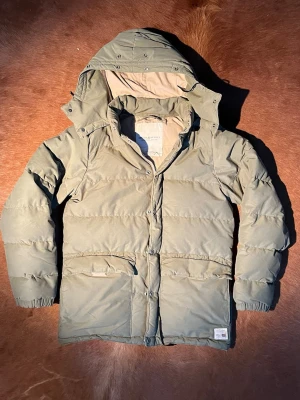 Olivgrön pufferjacka från Ralph Lauren - Olivgrön pufferjacka från Denim & Supply Ralph Lauren med huva, stora fickor och dragkedja med tryckknappar. Jackan är vadderad och har en avslappnad passform, perfekt för kalla dagar. Materialmix av bomull och nylon. Den har en fläck på ryggen men inget som stör. Storlek är S men sitter som en M/L🤠