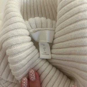 Vit ribbad polotröja från H&M - Säljer en supermjuk och ribbad polotröja från H&M i storlek S. Tröjan är vit, har hög polokrage och långa ärmar. Perfekt för lager på lager och riktigt snygg till både jeans och kjol. Materialet är stickat och ger en mysig känsla. Tycker att den sitter mer som en XS/S än S.