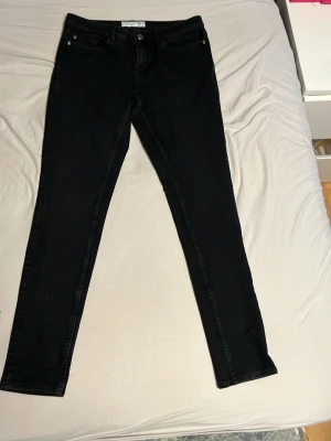 Svarta skinny jeans från Denim Department - Svarta jeans från Denim Department i storlek 40. Modellen är skinny med normal passform och klassisk femficksdesign. Jeansen har dragkedja och knapp framtill samt bälteshällor. Perfekta till sneakers eller boots.