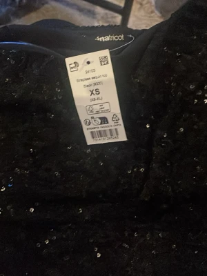 Svart paljett tubtopp från Gina Tricot - Säljer en svart tubtopp från Gina Tricot i storlek XS. Toppen är täckt med glitter.  toppen är axelbandslös.  Kan köpas med kjolen  också, hela summan för setter blir 630