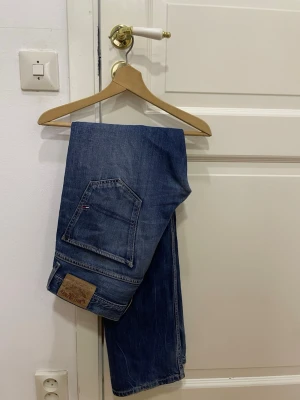 Straight blå vintage-jeans från Tommy Hilfiger - Säljer ett par blå vintage-jeans  från Tommy Hilfiger med snygga fickdetaljer och logotyp på bakfickan. Byxorna har raka ben och är gjorda i ett slitstarkt men mjukt jeanstyg. Jeansen är i acceptabelt skick men de är slitna, därav priset, men riktigt snygga. 