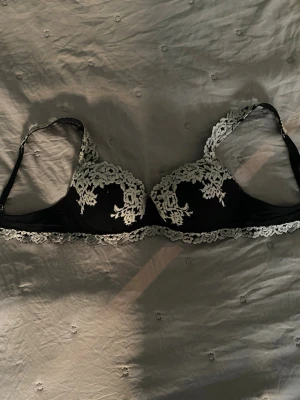 Svart spets-bh med blommig spets - Säljer en svart bh med vit blommig spetsdetalj från intimissimi. Jag säljer den för att den inte passar mig längre, den är i bra skick och den har inga hål.💞💞