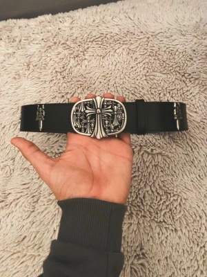 Crome hart bälte  - Säljer en svart väst från Crome hart med breda axelpartier och detaljerade silverspännen i form av kors och svärd längs framsidan. Västen är tillverkad i skinn och har en unik, edgy look med metallapplikationer som ger extra attityd.