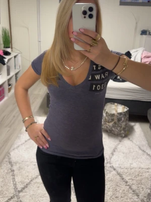 Mörklila t-shirt från G-Star RAW - Säljer en mörklila t-shirt från G-Star RAW i storlek XS. T-shirten har v-ringad hals, korta ärmar och tryck med siffror och text på bröstet. Materialet är mjuk bomull som sitter tight och följer kroppen. Perfekt för dig som gillar en enkel men snygg look.