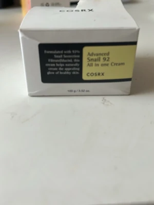 COSRX Advanced Snail 92 All in One Cream - En ansiktskräm med 92% snigelsekretfiltrat som ger huden en naturlig glow. Krämen kommer i en vit och svart förpackning med gul etikett och innehåller 100 g. Perfekt för dig som vill ha återfuktad och mjuk hud med extra lyster.