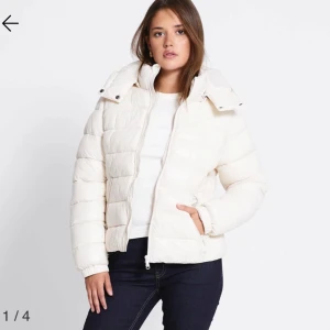 Vit pufferjacka med huva - Säljer en snygg vit pufferjacka med huva och dragkedja framtill. Jackan är quiltad och har en lite boxig passform med långa ärmar och elastiska muddar. Perfekt för kyliga dagar när du vill hålla dig varm och ändå se fräsch ut.