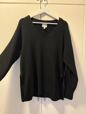Svart stickad tröja med v-ringning H&M - Svart stickad tröja från H&M i storlek XS. Tröjan har en djup v-ringning, långa ärmar och slits i sidorna för en chill look. Materialet är en mix av polyester, akryl, ull och elastan som gör den mjuk och skön. Perfekt för lager-på-lager under kyliga dagar.