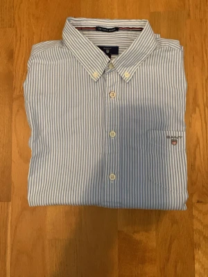 Blårandig skjorta från GANT - Snygg blårandig skjorta från GANT med klassisk button-down krage och vita knappar. Skjortan har lång ärm och bröstficka med broderad logga. Tillverkad i mjuk bomull som känns fräsch och lätt. Perfekt för dig som gillar stilrena och tidlösa plagg.