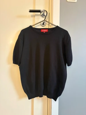 Svart stickad tröja från L.O.G.G. - Svart stickad tröja från L.O.G.G i storlek 158/164. med rund hals och korta ärmar. Tröjan har  ribbade muddar vid hals, ärmslut och nederkant.