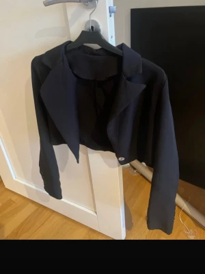Svart croppad kavaj med knappar - Snygg svart croppad kavaj med klassisk krage och långa ärmar. Kavajen har en knapp framtill och flera små knappar vid ärmsluten. Perfekt för dig som gillar stilrena och trendiga plagg med lite edge. Köpte den här på Plick precis men den passar mig inte. 