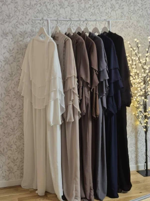 Långklänning med volang i flera färger - Säljer en elegant långklänning med flera lager volang upptill och långa ärmar. Finns i färgerna vit, beige, brun, grå, marinblå och svart. Klänningen har en loose passform och är tillverkad i ett lätt syntetmaterial som faller snyggt.