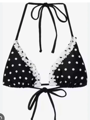 Svart prickig bikiniöverdel med volang - Säljer en svart bikiniöverdel med vita prickar och dekorativ vit volang längs kanterna. Modellen har knyt både i nacken och ryggen för justerbar passform. Perfekt för strandhäng och poolparty! OBS NOTERA ATT JAG SÄLJER ENDAST BIKINIÖVERDELEN. 