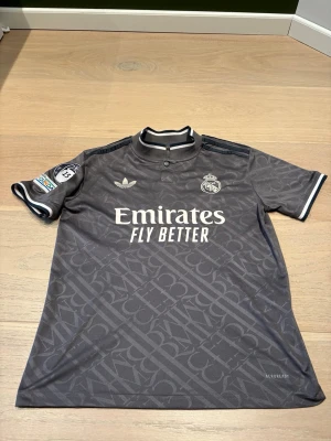 Real Madrid 24/25 Mbappe 9 - Bilderna visar en fotbollströja från Real Madrid med Mbappé och nummer 9 på ryggen, samt UEFA Foundation-märke på ärmen. Ingen sko syns på bilderna.