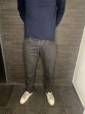 Levi's 501 mörkgrå jeans  - Säljer ett par klassiska Levi's 501 jeans i mörkgrå färg. Modellen har rak passform och normal midja, med fem fickor och knappgylf. Materialet är slitstark bomull och jeansen har den ikoniska Levi's-lappen bak i midjan.