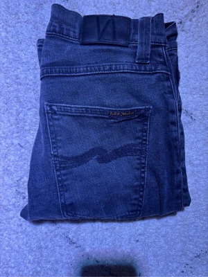 Svarta Nudie Jeans straight fit - Snygga svarta jeans från Nudie Jeans med klassisk femficksdesign och subtil vågdetalj på bakfickan. Modellen har rak passform och är tillverkad i slitstarkt bomullsmaterial. Storleken är W28L30