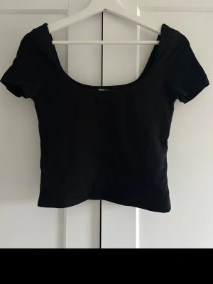 Topp - Säljer en svart croppad topp från Gina Tricot med korta ärmar och bred, rundad urringning.