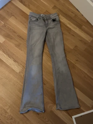 Grå bootcut jeans  - Snygga grå jeans med bootcut passform och klassisk femficksdesign. Jeansen har en låg midja och är tillverkade i mjukt jeanstyg som ger en skön känsla. Perfekta för dig som gillar retrovibbar och vill ha ett par jeans som sticker ut lite extra.