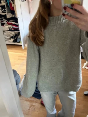 Grå stickad tröja med hög krage strl 176/S - Mysig grå stickad tröja med hög ribbad krage och långa ärmar. Tröjan har en loose passform och är perfekt för kyliga dagar. Enkel och stilren design som funkar till jeans eller andra favoritplagg. Storlek 176 men passar Xs/S