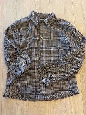 Rutig overshirt från weekday med bruna toner - Snygg overshirt med klassiskt rutigt mönster i bruna och beige toner. Jackan har knappar framtill och på ärmsluten, samt en passform. Perfekt att slänga på över en hoodie eller t-shirt för en chill look.