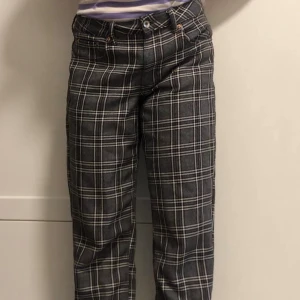 Grå rutiga raka byxor - Snygga grå byxor med vitt rutmönster och raka ben. Klassisk femficksmodell med bälteshällor och knappstängning. Perfekta för dig som gillar en stilren och trendig look.