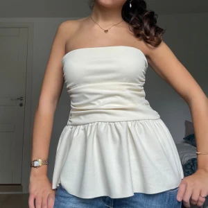 Ljusgul/ beige peplum tubtopp - Säljer en tubtopp med peplumvolang nedtill. Toppen är axelbandslös och har en bandeauformad överdel som sitter tight över bysten.