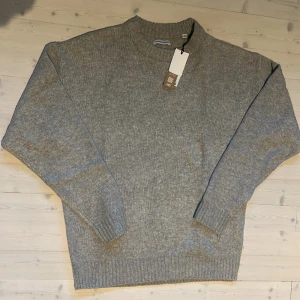 Grå stickad tröja från Jack & Jones - Mysig grå stickad tröja från Jack & Jones i storlek M. Tröjan har rund halsringning, ribbade muddar och är tillverkad i ett mjukt material som passar perfekt för kyligare dagar. Enkel och stilren. Helt splitterny och oanvänd!              Säljer pga att den inte passar mig och jag fick den i present utan kvitto😕